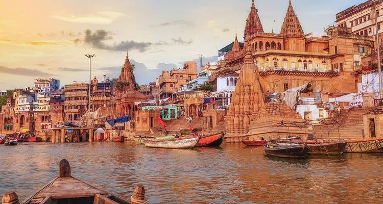 Vue des ghats de Varanasi au coucher du soleil avec des bateaux sur la rivière.