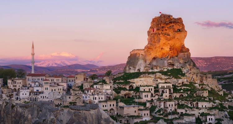 Rotsforten van Cappadocië die warm glanst in het schemerdonker en uitkijkt over in de rotswand uitgehouwen huizen