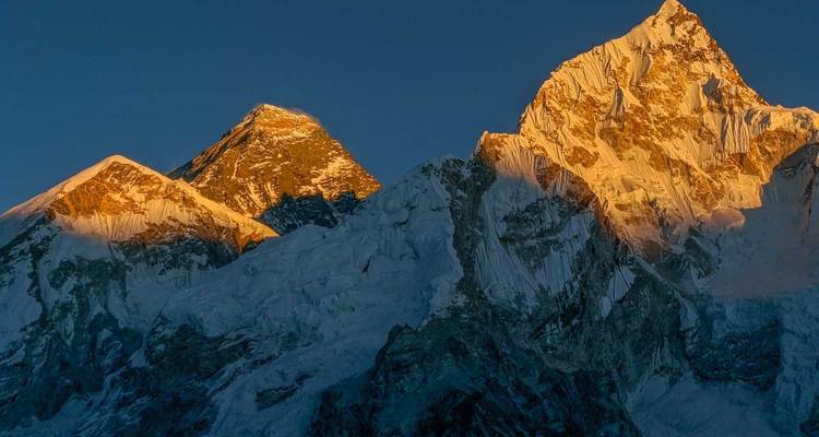 Mount Everest en omliggende pieken bij zonsopgang met oranje gloed.