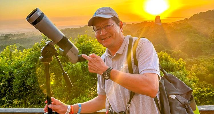 Un hombre señala a un telescopio en un mirador del amanecer de la selva con la silueta de una pirámide del templo detrás de él.