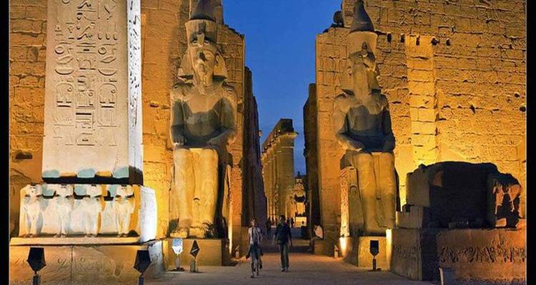Magníficas ruinas iluminadas con dos personas caminando por un templo egipcio durante la noche.