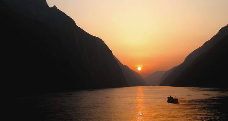 Sunset over a serene river between silhouette mountains.