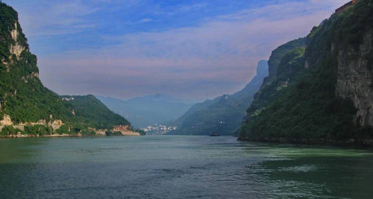 Tranquil river flanked by green-clad cliffs under a blue sky.