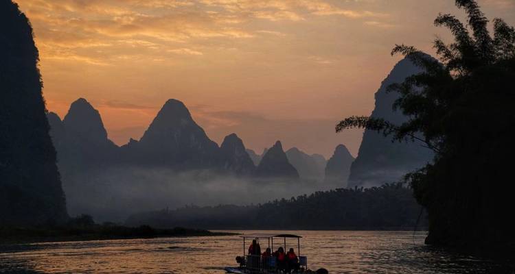 A scenic view of karst mountains and a small boat on the Li River during sunset.