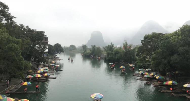 River scene with colorful umbrellas on rafts in a misty karst landscape.