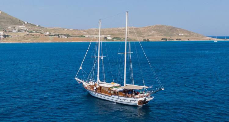 A sailing yacht in the open sea with hills in the background.