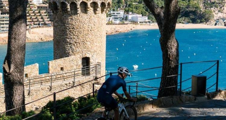 Cyclist on a path with a scenic view of a coastal town and the sea.