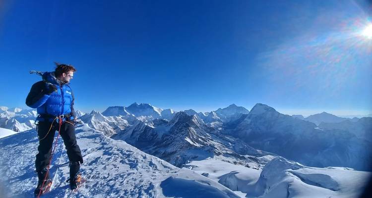 Avonturier op besneeuwde bergtop, uitgestrekt berglandschap verlicht door de zon.