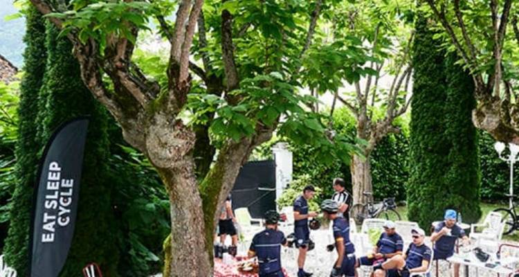Cyclists gathering in a shaded area with trees.