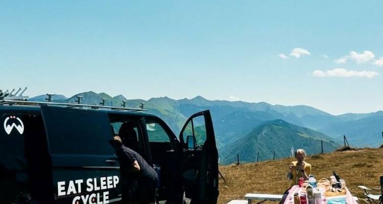 Cyclists near a van with mountains in the background.
