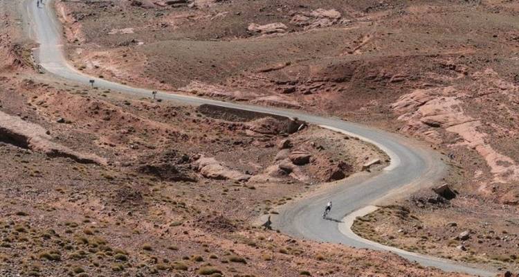 Winding road in a desert-like setting with cyclists.