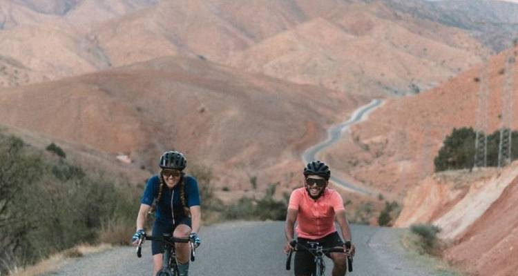 Two cyclists on a road with desert hills in the background.