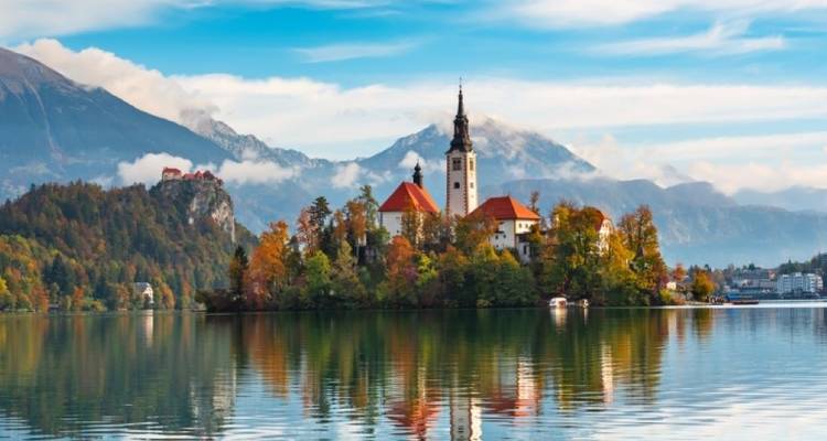 Scenic view of an island with a church on a lake, surrounded by mountains.
