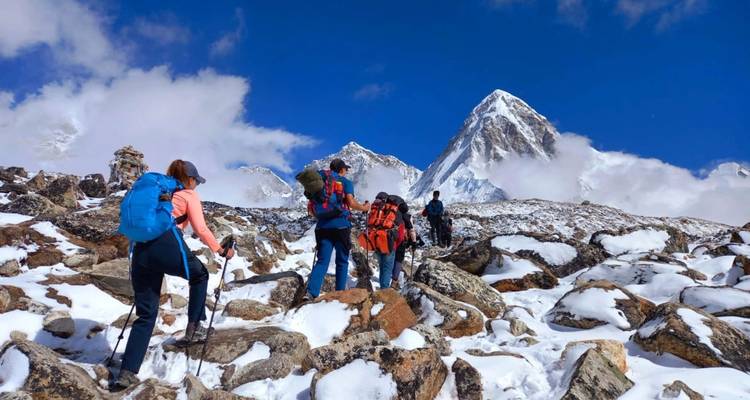 Wandelaars die trekken naar een besneeuwde top onder blauwe luchten.