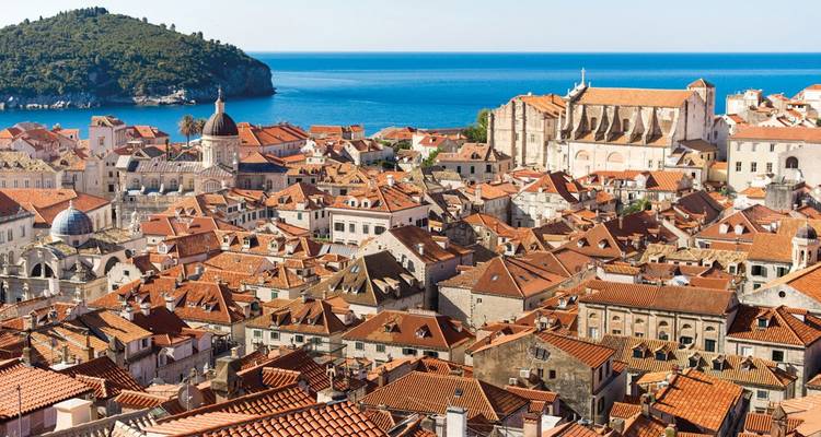 Vista panorámica de una ciudad costera histórica con tejados de terracota y mar azul cristalino.