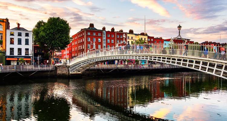 El Puente Ha'penny se arquea sobre el río Liffey con los coloridos edificios de Dublín reflejados en el agua al atardecer.