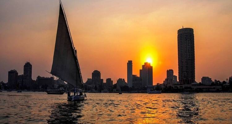 Voilier sur une rivière au coucher du soleil avec horizon urbain