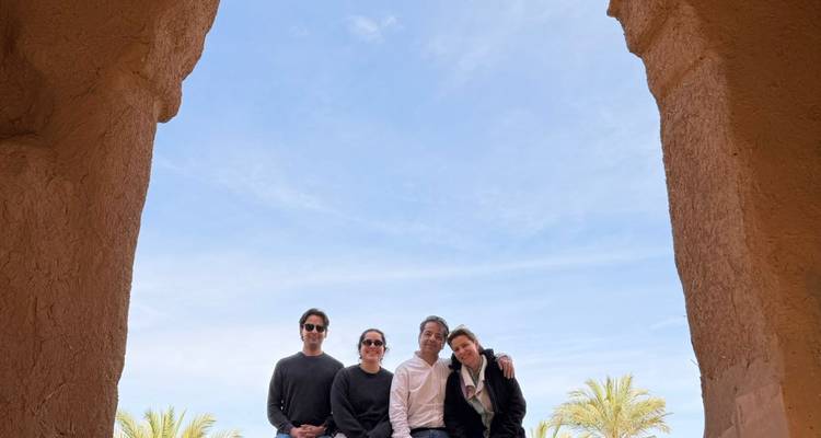 Groep staand in een booggang met uitzicht op palmbomen.