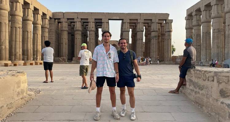 Des voyageurs posant devant d'imposantes colonnes de grès dans un temple égyptien antique.