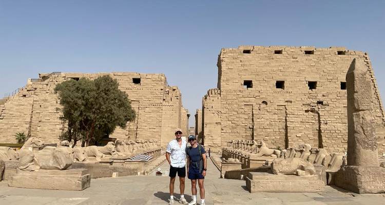 Deux touristes se tenant parmi les sphinx à tête de bélier et les murs de pierre massifs du temple de Karnak.
