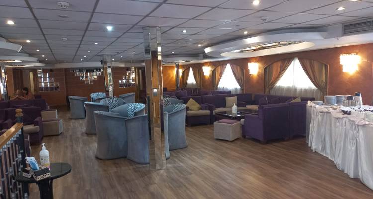 Grand salon spacieux sur un navire de croisière fluviale avec des canapés violets et un revêtement de sol en bois.