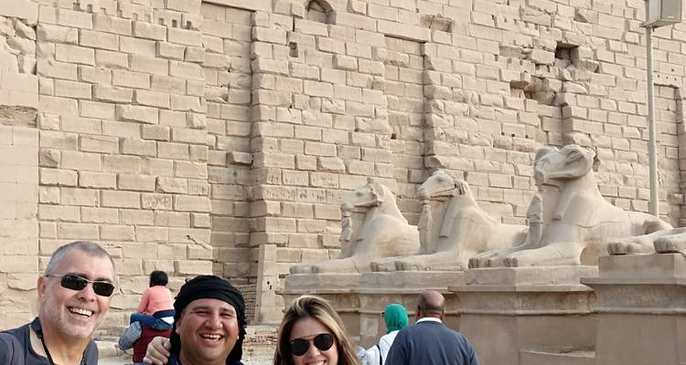 Des touristes souriants à côté de statues de sphinx à tête de bélier taillées dans le grès.