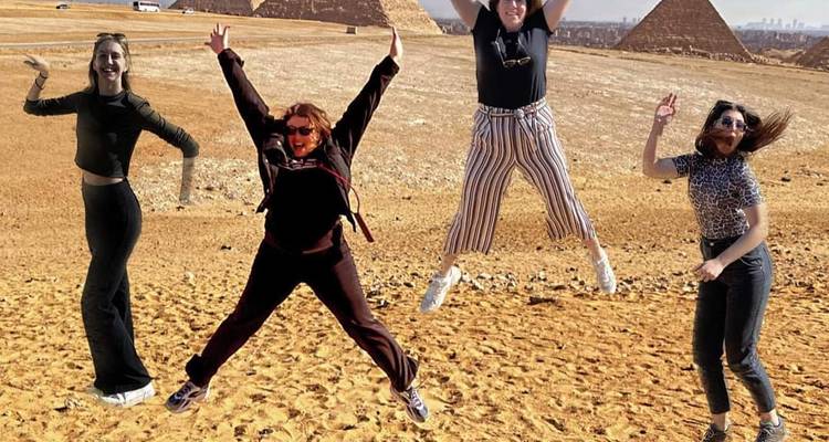 Quatre femmes sautant dans le désert avec les Pyramides de Giza en arrière-plan.