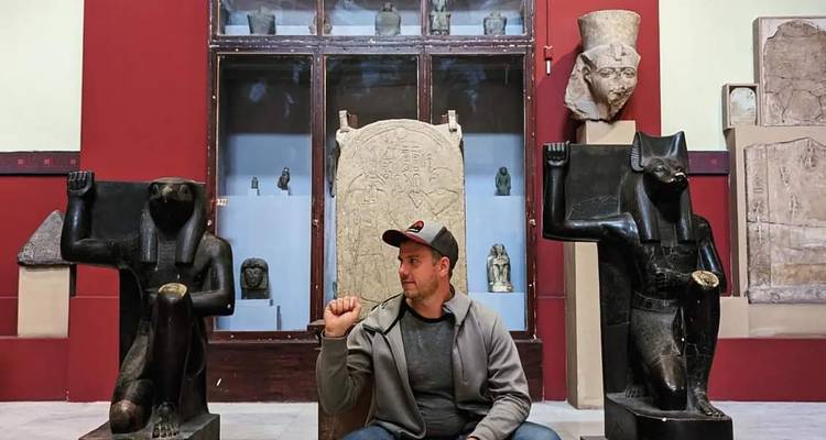 Un visiteur assis entre deux statues de divinités égyptiennes anciennes dans une salle de musée.
