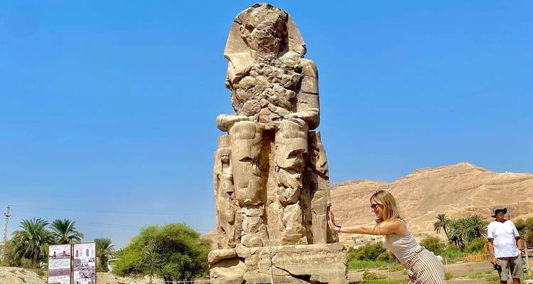 Voyageur poussant de manière ludique contre la statue du Colosse de Memnon à Louxor.