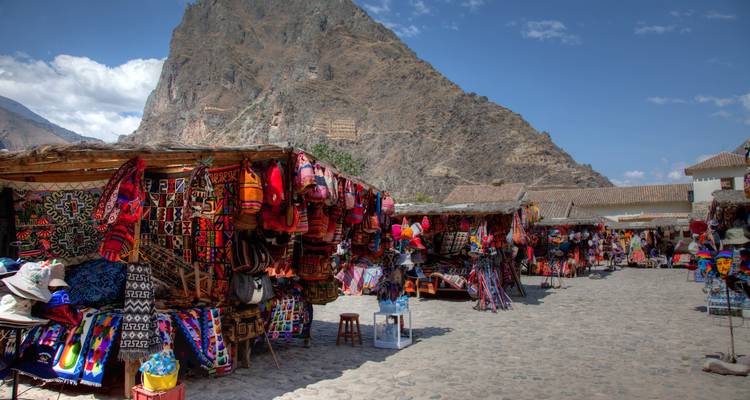 Market in Ollantaytambo with colorful textiles and a mountain backdrop.