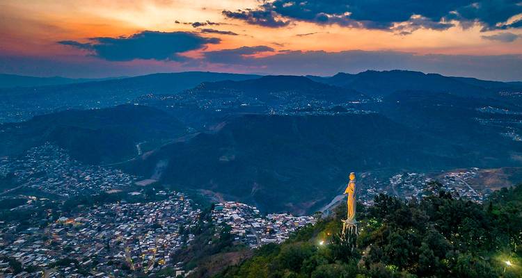 Une vue aérienne d'une ville avec une grande statue au premier plan au coucher du soleil.