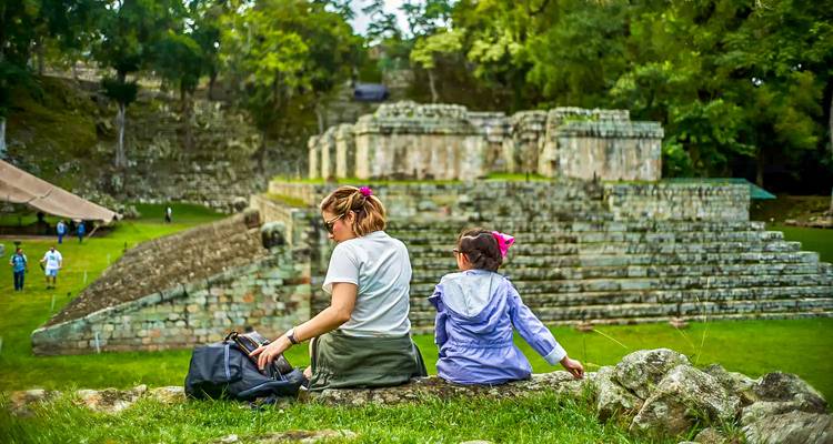 Une famille assise sur une zone herbeuse avec vue sur des ruines antiques.