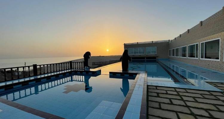 Infinity-Pool auf dem Dach mit Meerblick bei Sonnenuntergang und zwei in Silhouette dargestellten Gästen.