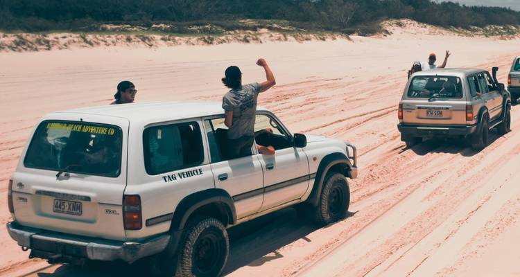 Deux véhicules tout-terrain roulant sur une plage de sable avec des gens qui font signe depuis les toits ouvrants.