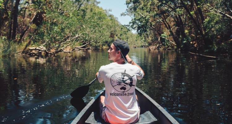 Une personne pagayant en canoë sur une rivière calme entourée d'une végétation luxuriante.