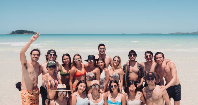 Un groupe de personnes posant sur une plage avec de l'eau turquoise et un ciel dégagé.
