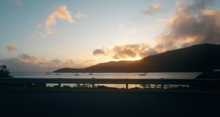 Une vue de coucher de soleil sur l'océan avec des bateaux et des montagnes au loin.
