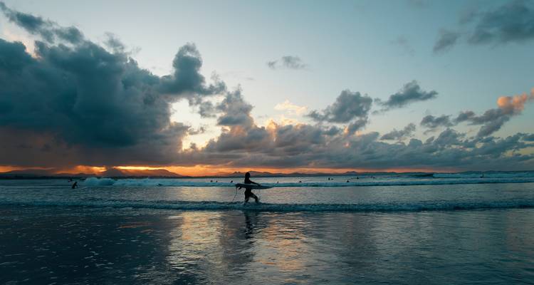 Un surfeur marchant le long de la plage au coucher du soleil avec des vagues en arrière-plan.