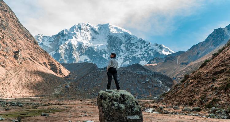 Personne debout sur un rocher avec des montagnes enneigées en arrière-plan.