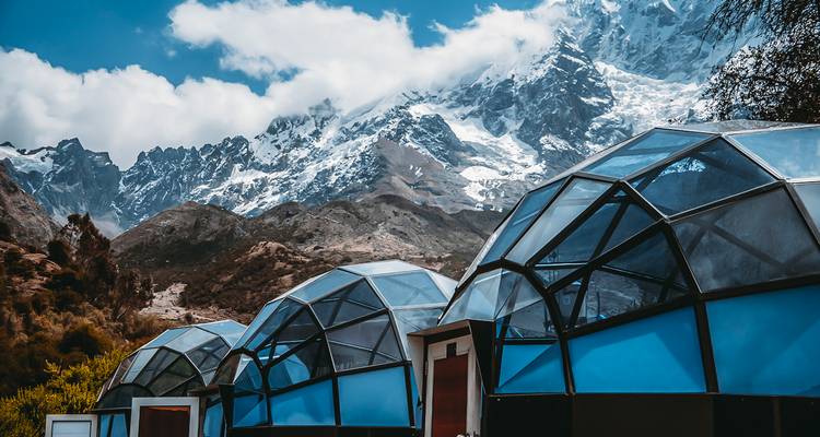 Dômes géodésiques sur un site de camping en haute altitude avec des sommets enneigés en arrière-plan.