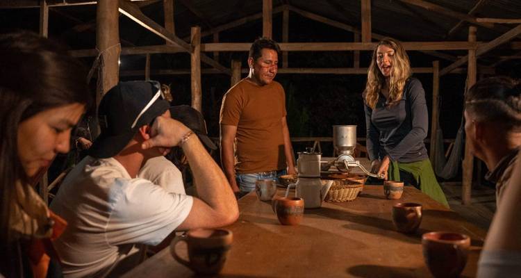 Personas reunidas alrededor de una mesa, posiblemente comiendo o teniendo una discusión, en una estructura de madera.