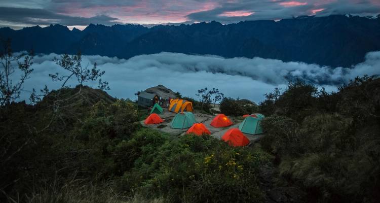 Kampeerterrein met kleurrijke tenten boven een zee van wolken bij zonsondergang.
