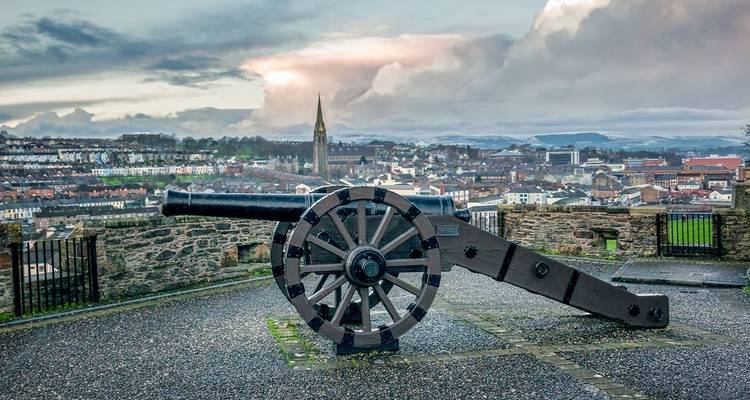 Historisch kanon op de stadsmuren met uitzicht over de daken van Londonderry onder een dramatische hemel