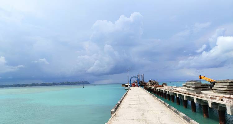 Jetée s'étendant dans des eaux bleu clair sous un ciel nuageux.