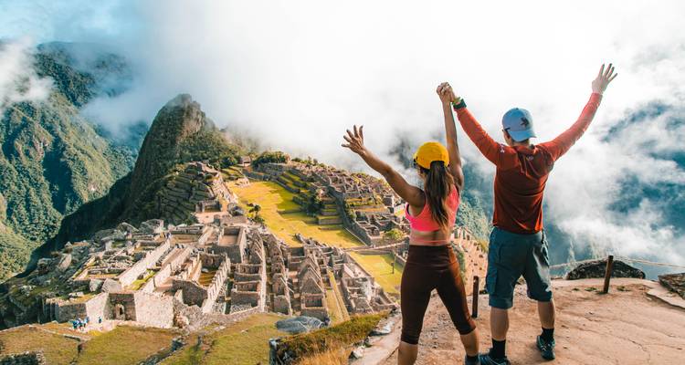 Twee mensen die vieren met opgeheven handen met uitzicht op Machu Picchu.