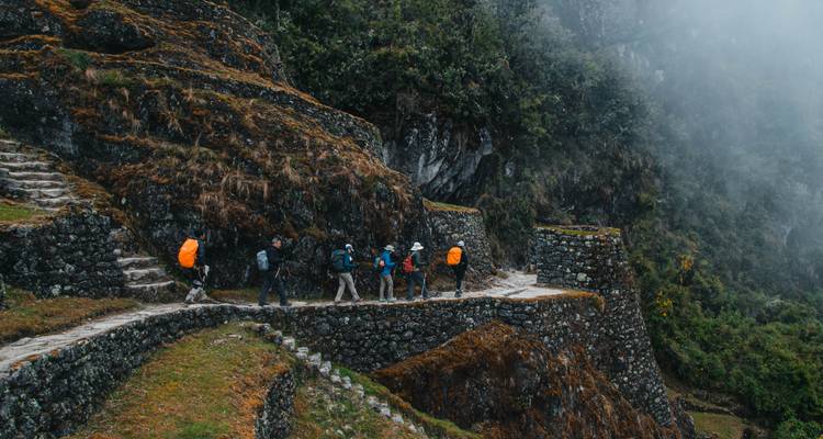 Wandelaars die langs een oud stenen pad lopen in een weelderige omgeving.