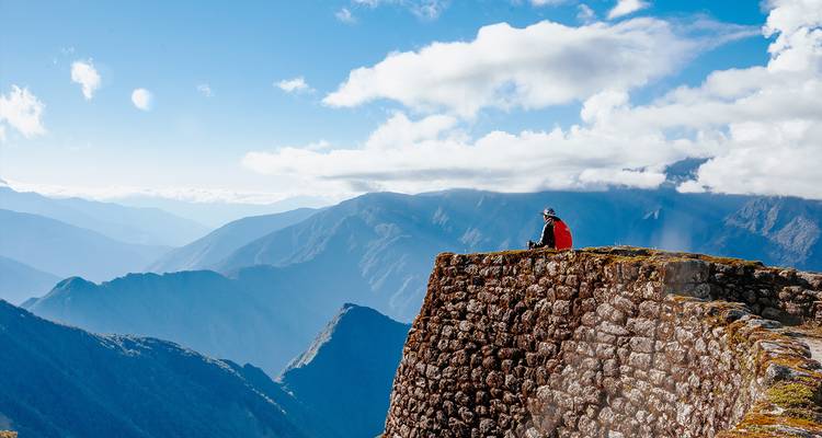 Persoon zittend op een stenen muur genietend van het uitgestrekte bergzicht.
