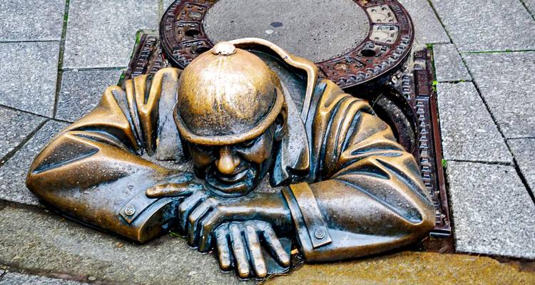 Estatua de bronce emergiendo de una alcantarilla en una calle empapada por la lluvia.