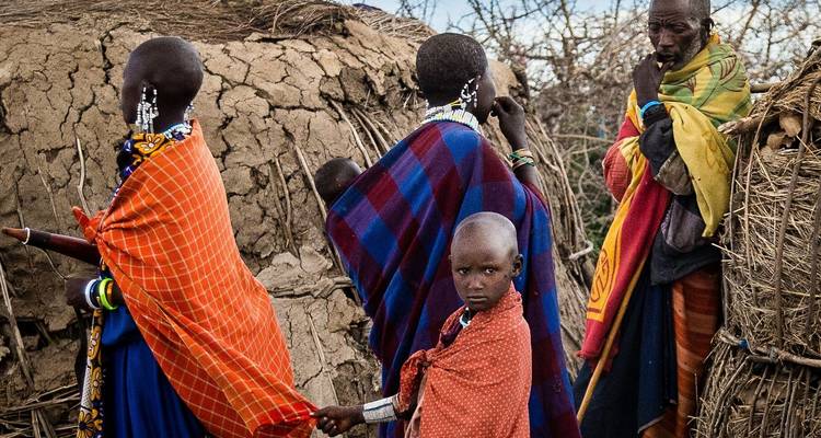 Groep mensen in traditionele kleding buiten een modderhut.