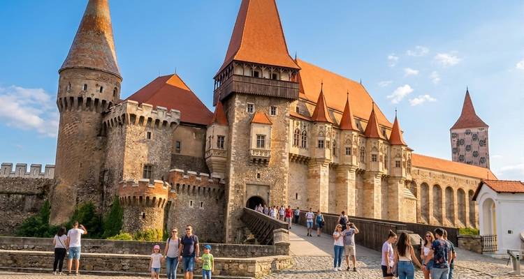 Bezoekers die de middeleeuwse torens en rood betegelde daken van Kasteel Corvin verkennen onder een heldere hemel
